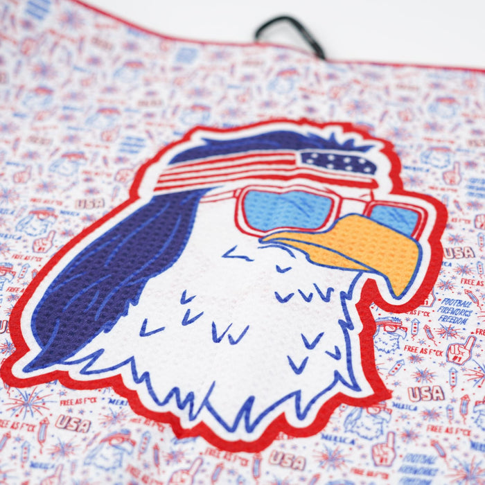 Close-up of a cartoon bald eagle in red sunglasses and stars-and-stripes headband is outlined in red on the 'Merica - Towel, a 2-sided microfiber towel with USA icons, “USA,” “Free as F*ck,” peace signs, and fireworks—perfectly patriotic for the gym.