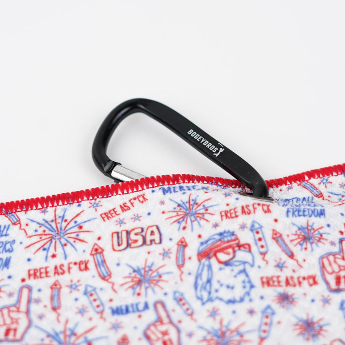 A close-up of the 'Merica - Towel, a red, white, and blue microfiber gym towel with fireworks, peace signs, USA, and FREE AS F*CK prints. It has red-stitched edges, a black “BOGEY BOYS” carabiner clip, and double-sided design.